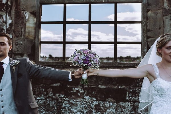 Bride and groom with arms outstretched holding bouquet