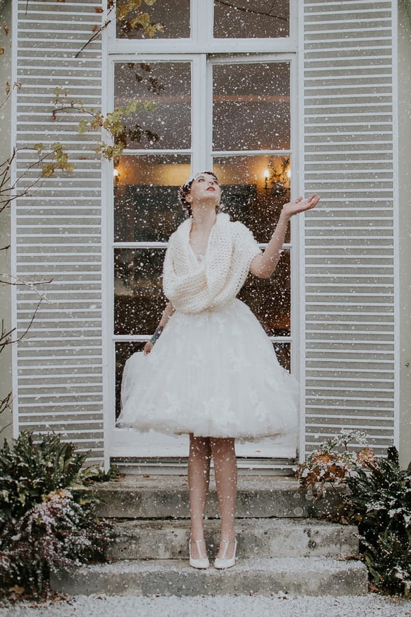 Bride holding out hand as snow falls