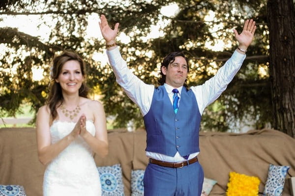 Groom holding arms up for applause after speech