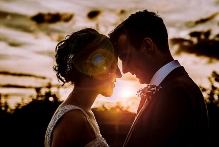 Bride and groom touching heads with sun shining between them