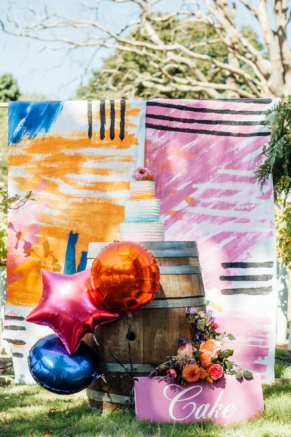 Wedding cake on barrel against colourful wedding backdrop