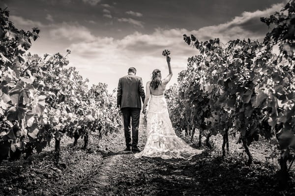 Bride holding bouquet in the air as she walks through vineyard with groom - Picture by Cinderella Photographie