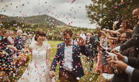 Bride and groom smiling as they walk through a shower of colourful confetti - Picture by Neil Jackson Photographic