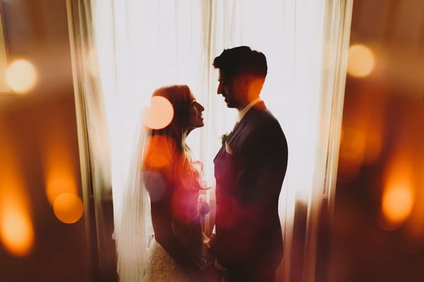 Bride and groom facing each other in front of curtain covered window - Picture by Luke Hayden Photography