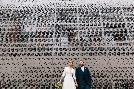 Bride and groom holding hands in front of funky squared backdrop - Picture by Eclection Photography