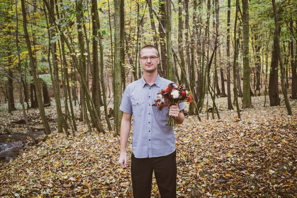 Beat man holding bouquet in forest