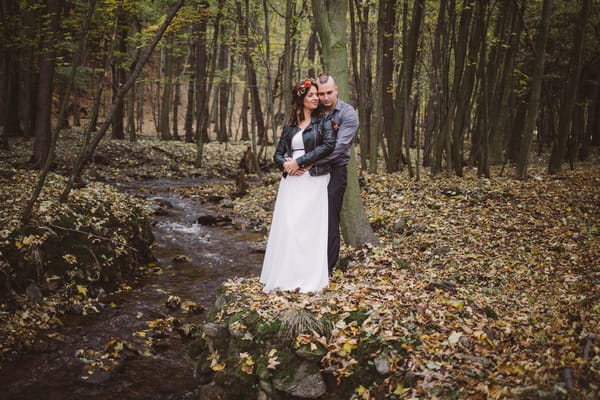 Groom with arms around bride from behind next to stream