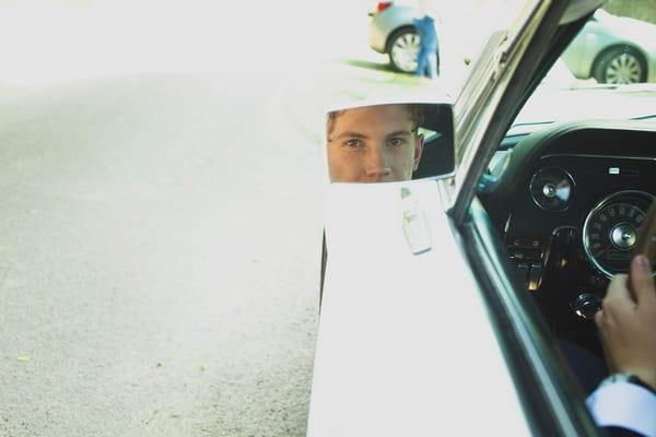 Groom's reflection in wedding car wing mirror