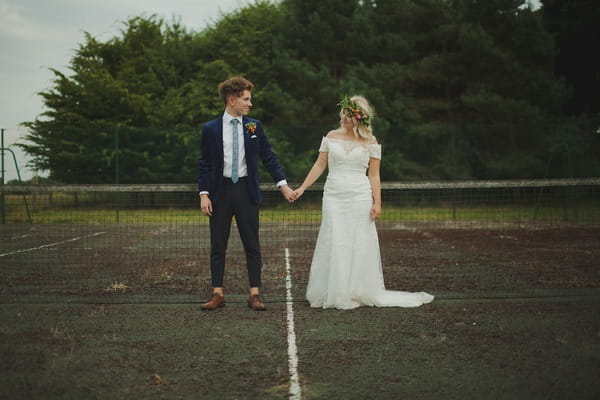 Bride and groom holding hands on tennis court