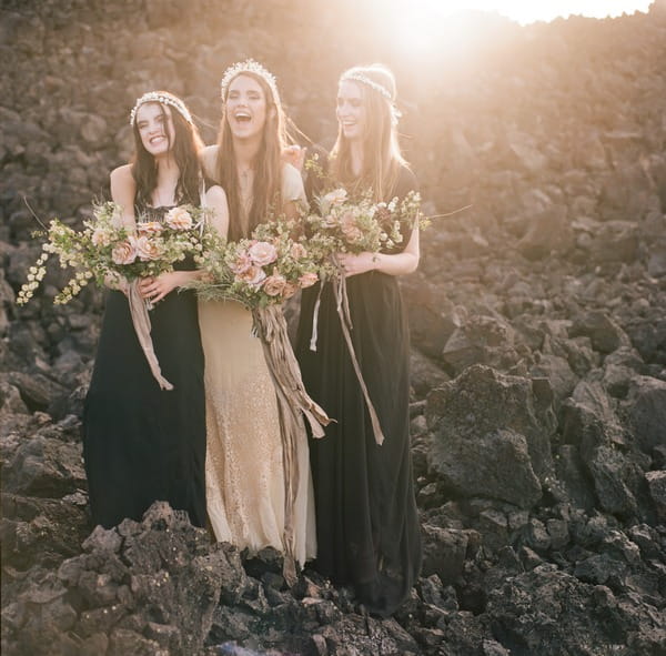 Three boho brides laughing together on rocks