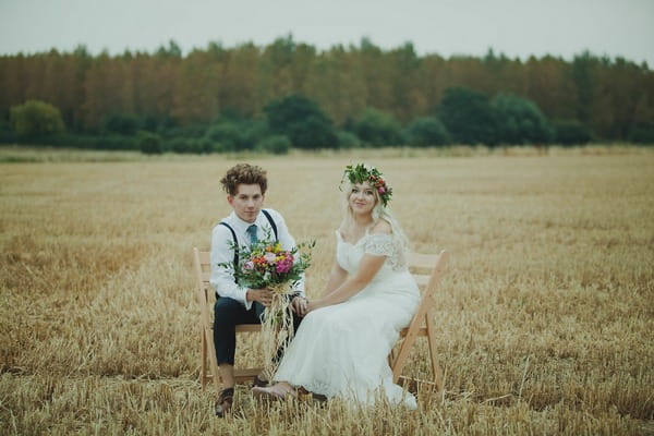 Bride and groom sitting on chairs in corn field