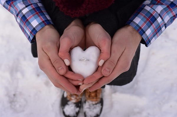 Couple holding engagement ring in snow