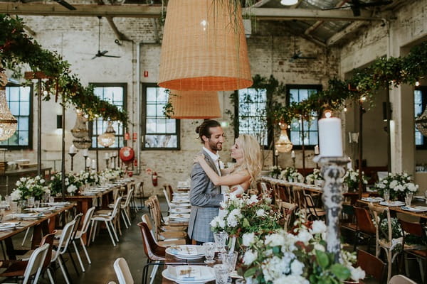 Bride and groom standing in middle of tables of warehouse wedding