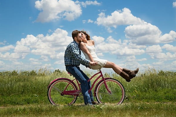 Woman kissing man whilst sitting on handlebars of bicycle