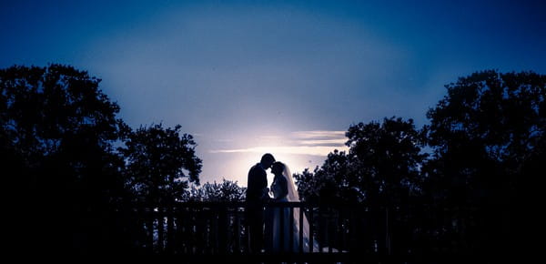 Silhouette of bride and groom standing on bridge at night - Picture by Moritz Schmittat Photography