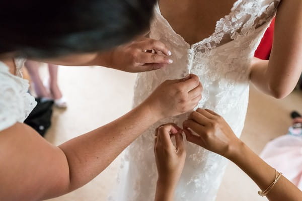 Bridesmaids fastening back of bride's dress