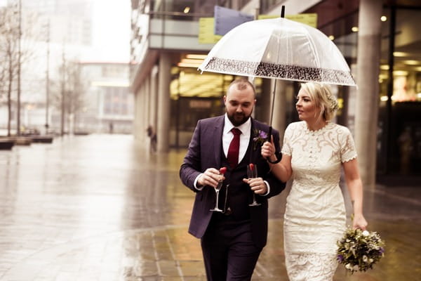 Bride and groom walking in rain with umbrella