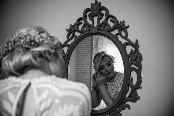 Bride looking in mirror to put earrings on