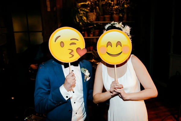Bride and groom holding emoji face masks over their faces