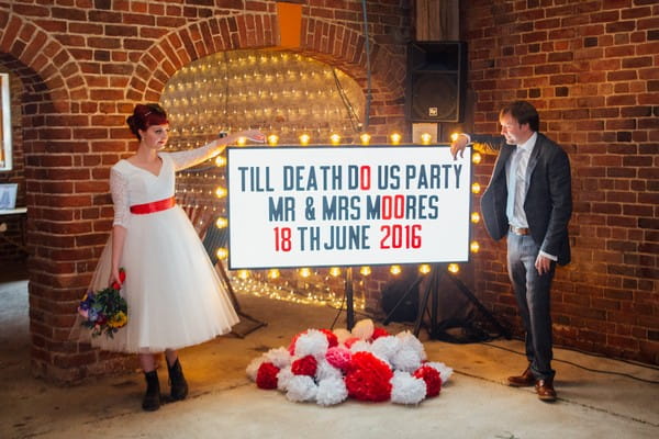 Bride and groom standing next to Till Death Do Us Party illuminated sign