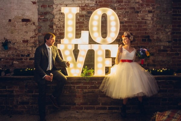 Bride and groom sitting next to illuminated LOVE letters