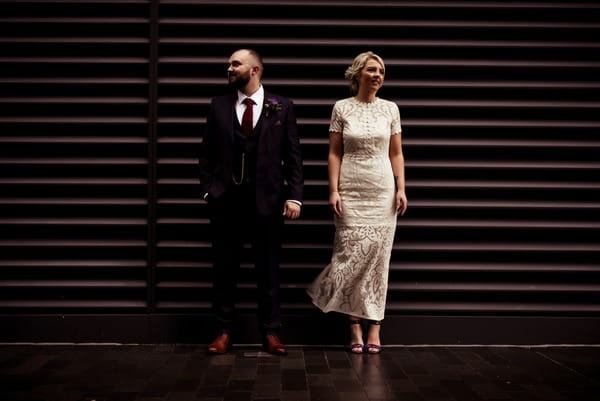 Bride and groom standing up against shop shutter