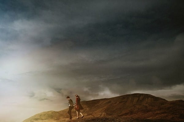 Bride and groom walking on top of hill below dark clouds - Picture by Rubistyle Photography