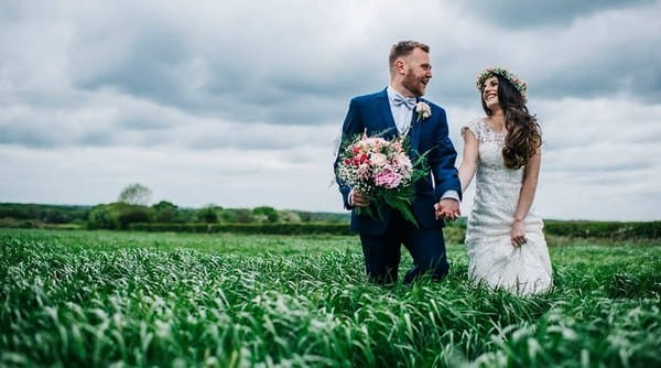 Bride and groom in field with groom holding bride's bouquet - Picture by Kerry Woods Photography