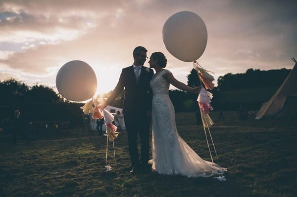 Bride and groom holding balloons as the sun sets - Picture by Naomi Jane Photography