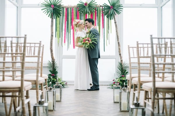 Bride and groom in front of pink and green wedding backdrop