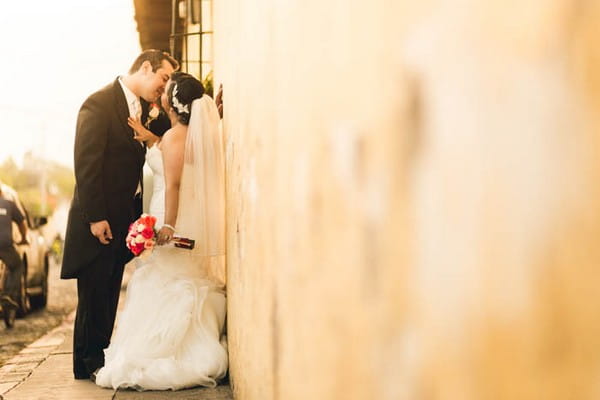Bride and groom kissing against wall