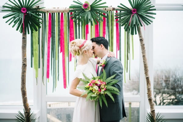 Bride and groom kissing in front of pink and green backdrop