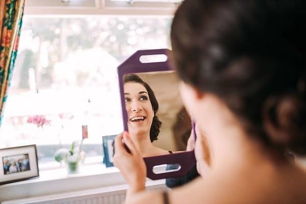 Bridesmaid smiling as she looks in mirror to see make-up