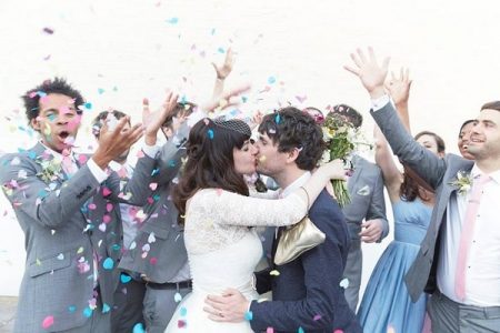 Bride and groom kissing as wedding guests throw confetti over them - Picture by Natalie J Weddings