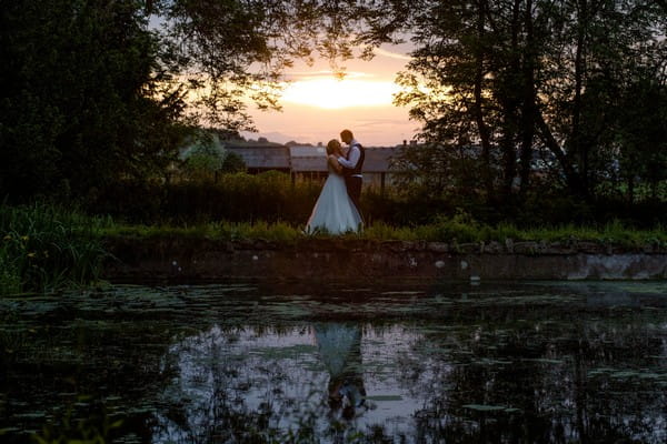 Bride and groom standing by pond in evening - Picture by Nicola Gough Photography