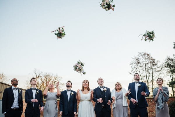 Bridal party standing in line as bride and bridesmaids throw bouquets in the air - Picture by Andrew Craner Photography