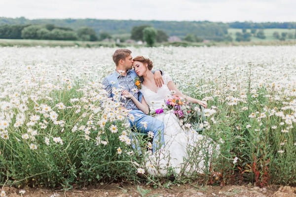 Bride and groom sitting in a field of daisies - Picture by Jo Bradbury Photography
