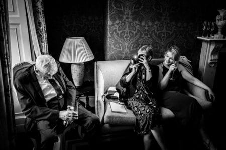 Woman taking picture of man who has fallen asleep in his chair at a wedding - Picture by How Photography
