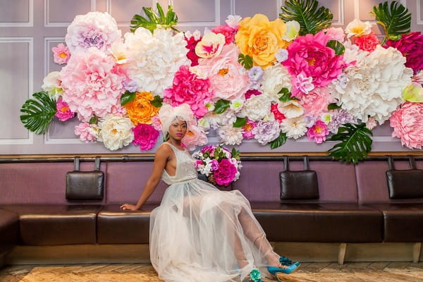 Bride sitting in front of bright and colourful flower wall