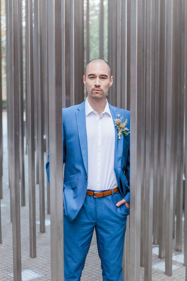 Groom in blue suit standing between poles