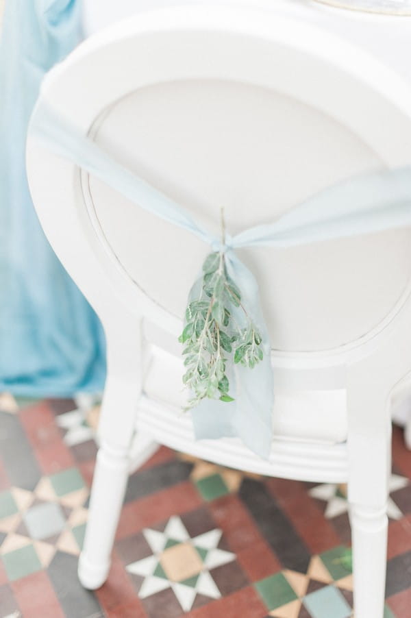 Light blue ribbon and foliage tied to back of wedding chair