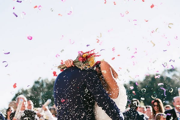 Bride and groom hugging as confetti falls around them - Picture by Sara Lobla