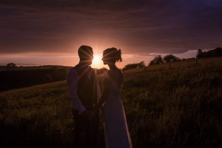 Bride and groom holding hands at sunset with the sun shining between their heads - Picture by Chris Kemp Photography