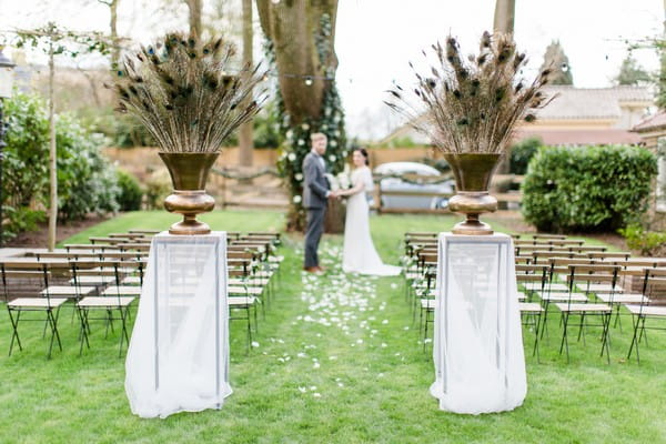 Large urns of peacock feathers at entrance to wedding ceremony
