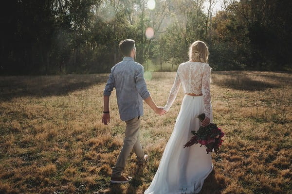 Bride and groom walking across field holding hands