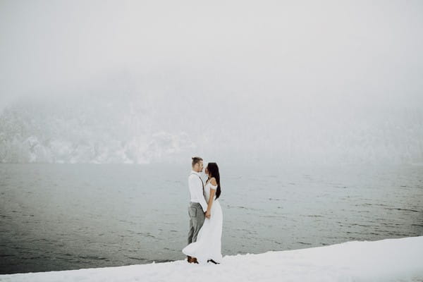 Couple standing in snow next to water
