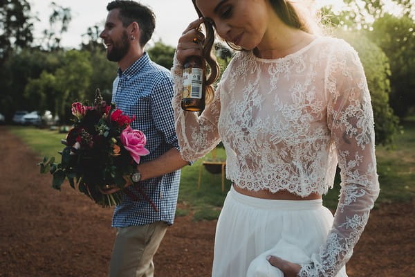 Bride holding bottle of beer and groom holding bouquet