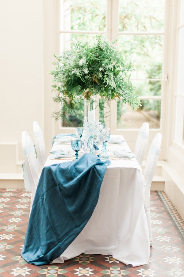 Long wedding table with Blue runner and large foliage centrepiece