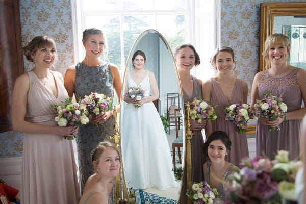 Bridesmaids standing next to mirror with bride's reflection