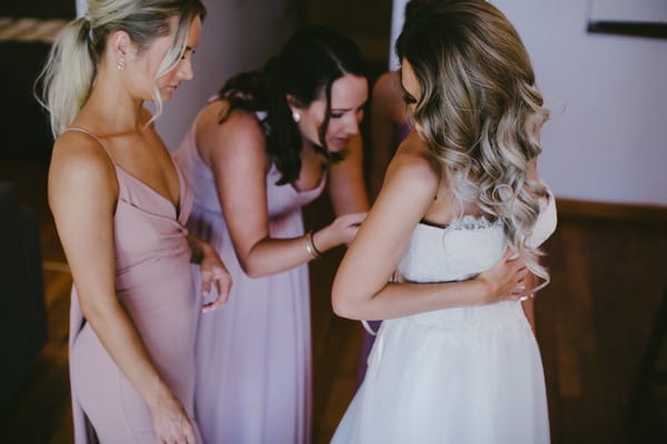 Bridesmaids doing up back of bride's wedding dress